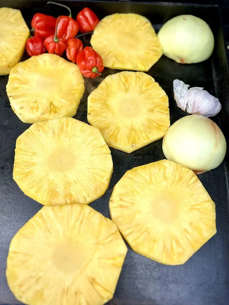 Charred habanero peppers and pineapple ingredients on the griddle for the preparation of a deliciously hot and sweet salsa